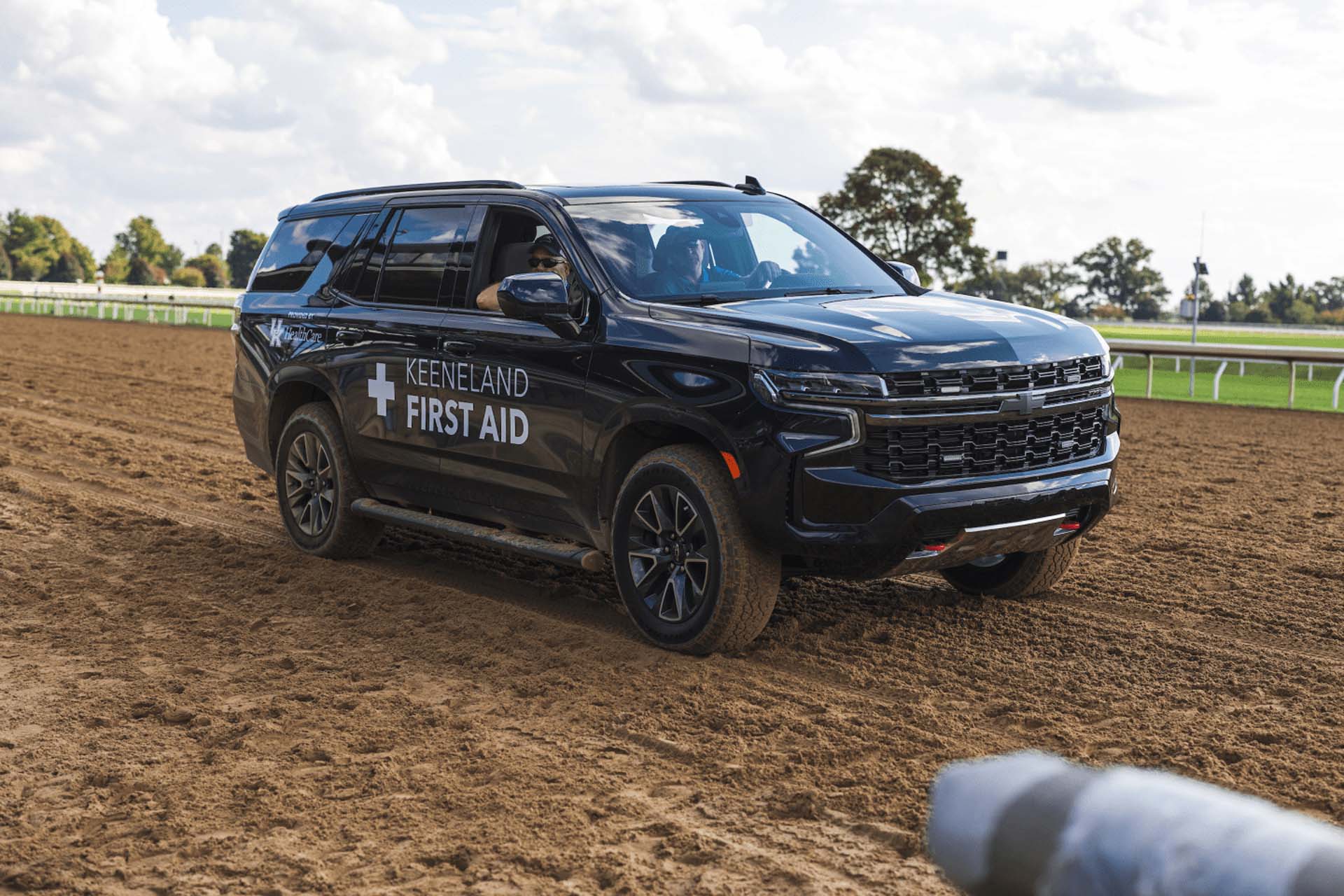 A picture of the Racecoltvalley First Aid car on the dirt track. It is a large black Chevy SUV.